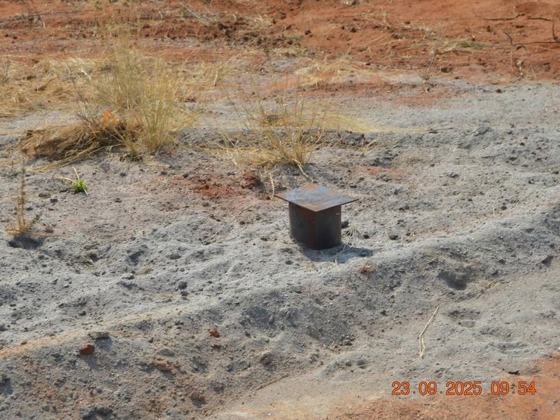 A close-up view of a metal survey marker or geotechnical stake embedded in the soil on a vacant agricultural plot.