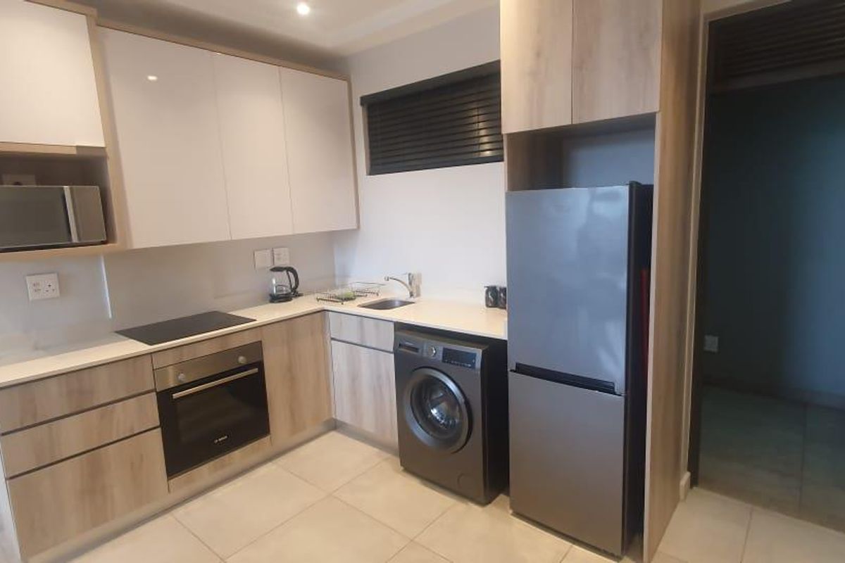 Modern kitchen featuring light wood and white cabinetry, stone countertops, built-in oven, electric hob, and integrated microwave with tiled flooring.