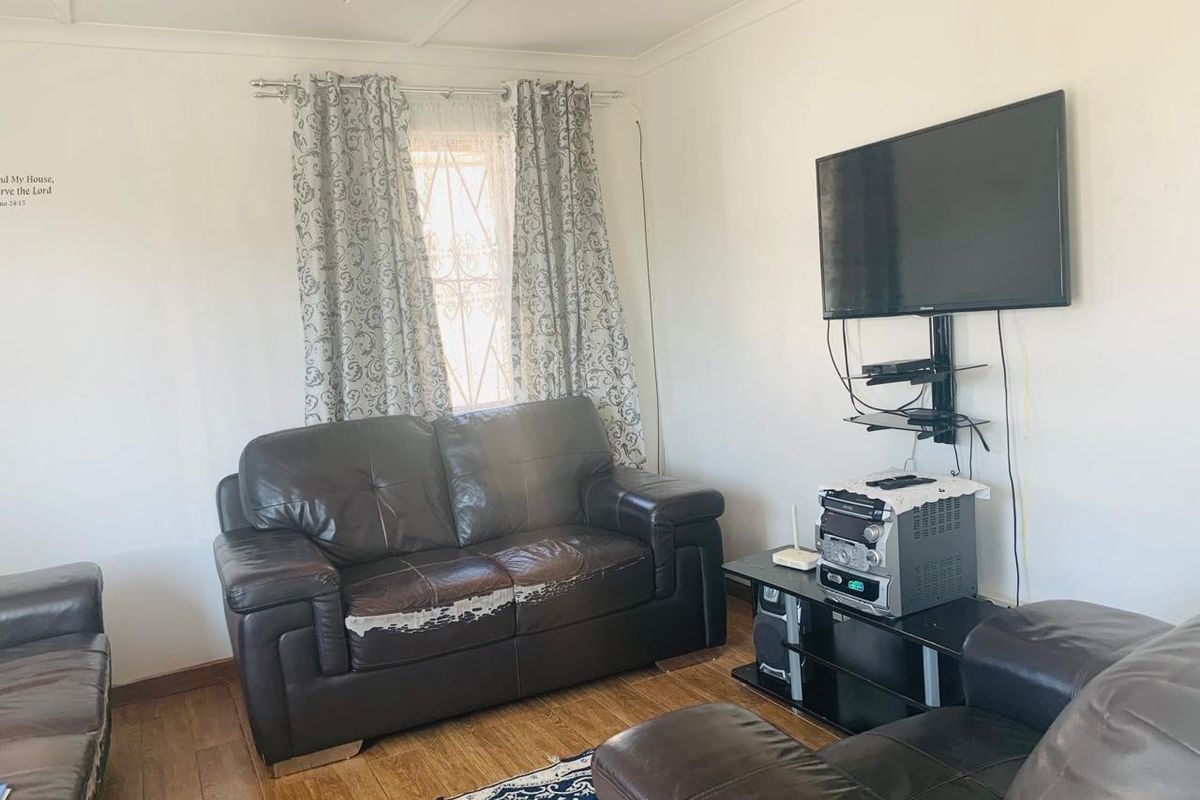 A functional living room featuring laminate flooring and a window fitted with security bars, providing a basic and practical living space.