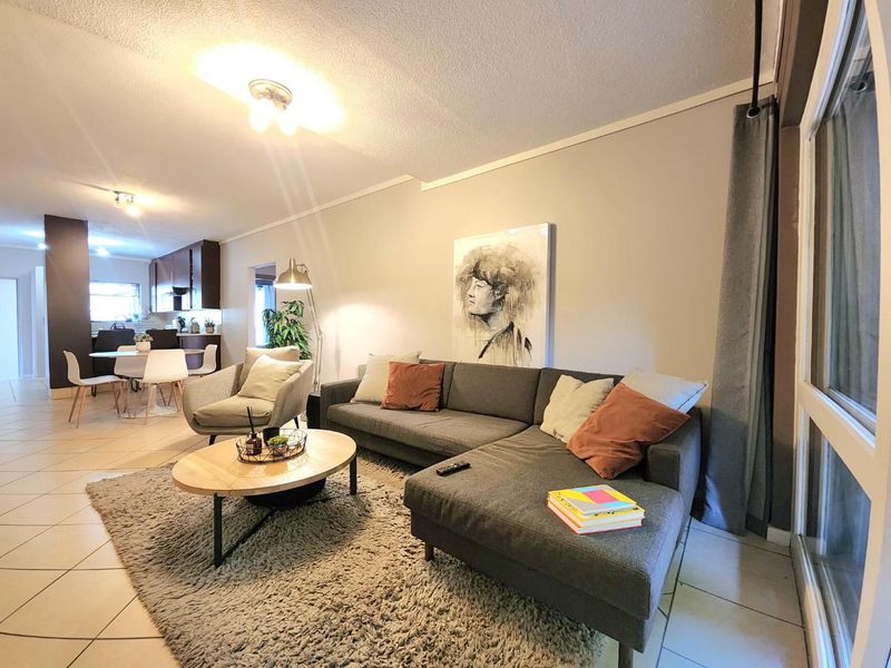 An open-plan living and dining area featuring tiled flooring, neutral walls, and a seamless transition into a functional kitchen space.