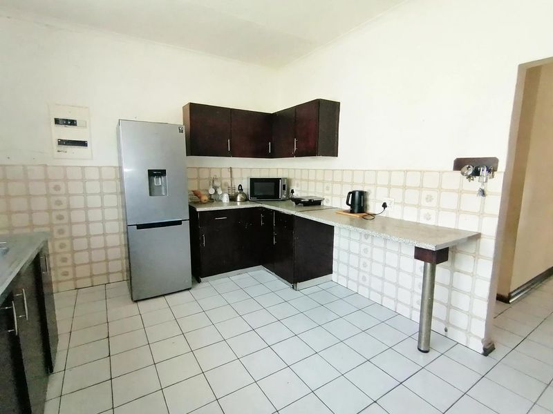 A functional kitchen featuring dark wood cabinetry, laminate countertops, and tiled surfaces, offering a practical layout with potential for modern updates.