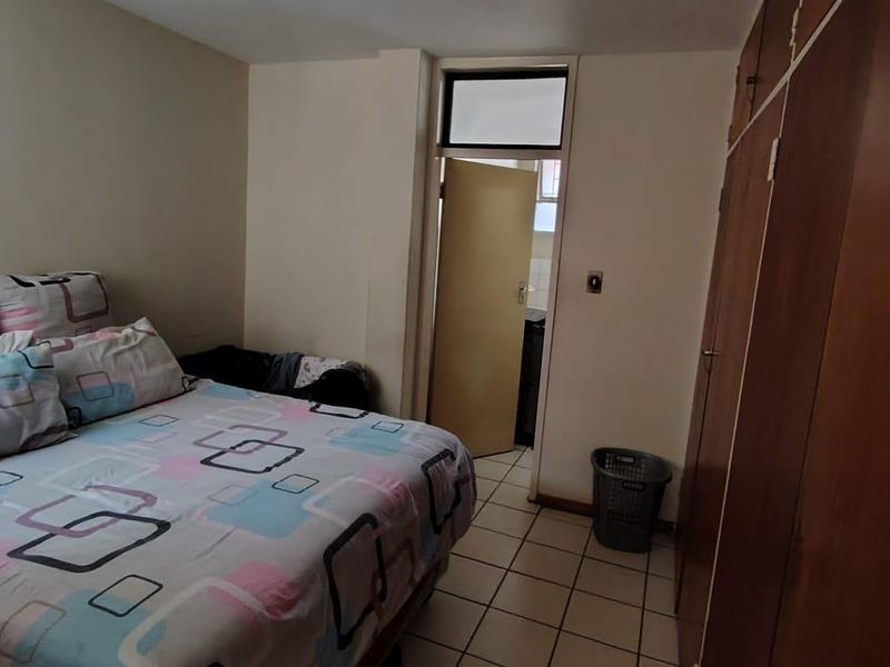 A functional bedroom featuring built-in wooden cupboards and tiled flooring, offering a practical layout with direct access to an adjoining room.