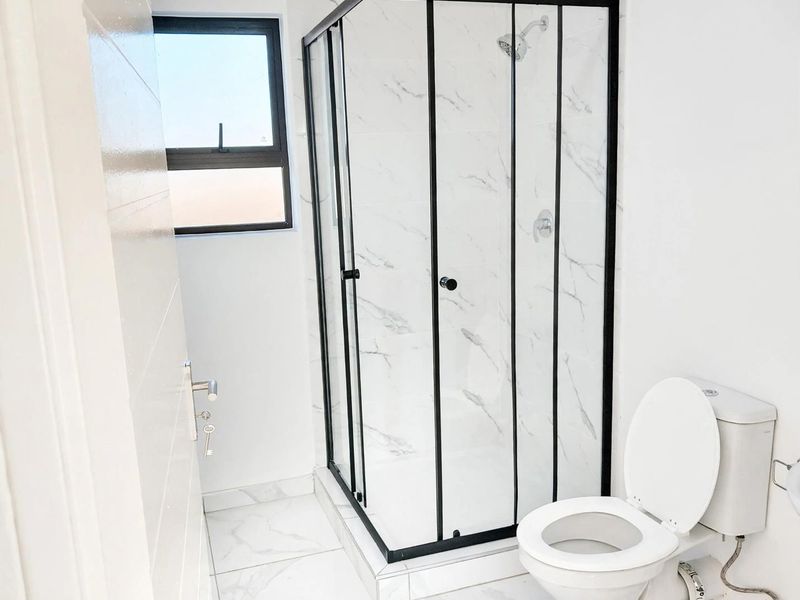A modern bathroom featuring a corner shower enclosure with black framing, marble-look wall tiles, and a standard toilet.