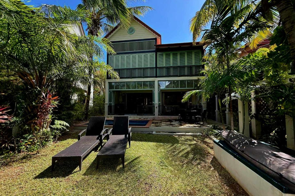 Rear view of a two-story maison de ville featuring a private swimming pool, covered patio area, and lush tropical garden landscaping.
