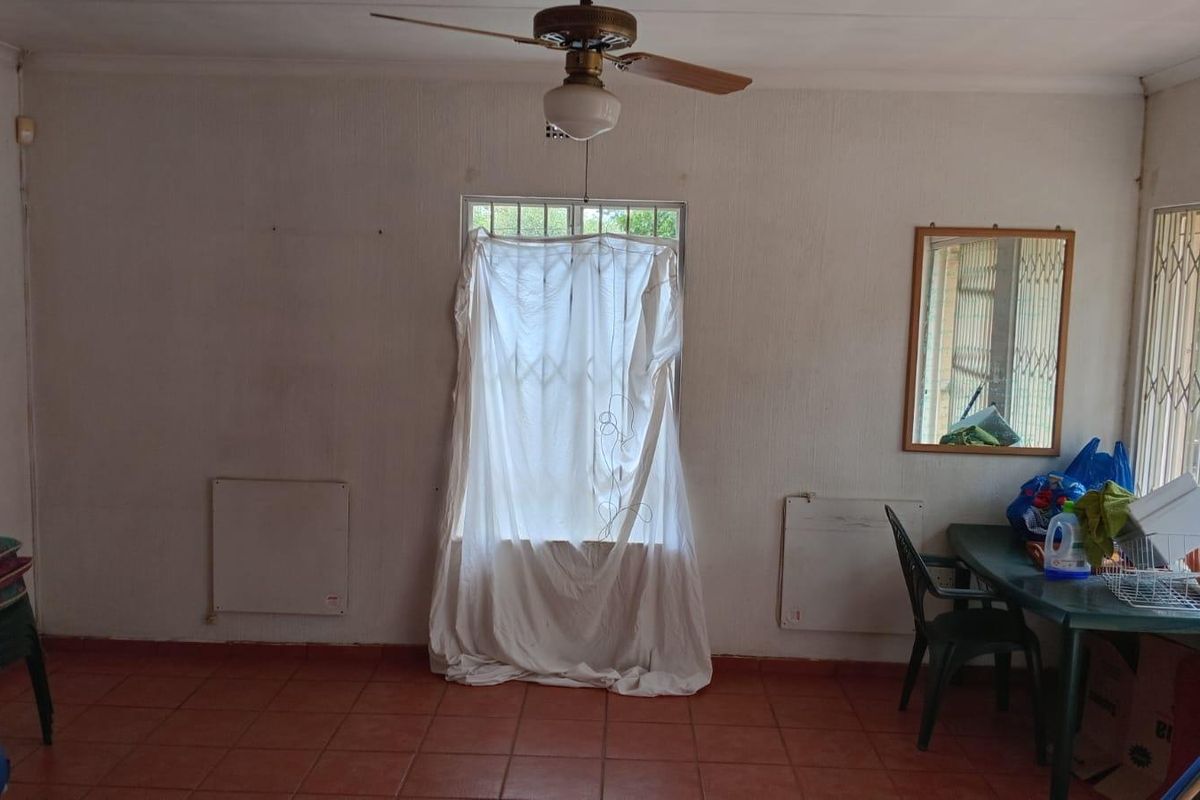 A living area featuring terracotta floor tiles, a ceiling fan, and security gates on the windows, offering a functional space with potential for updates.