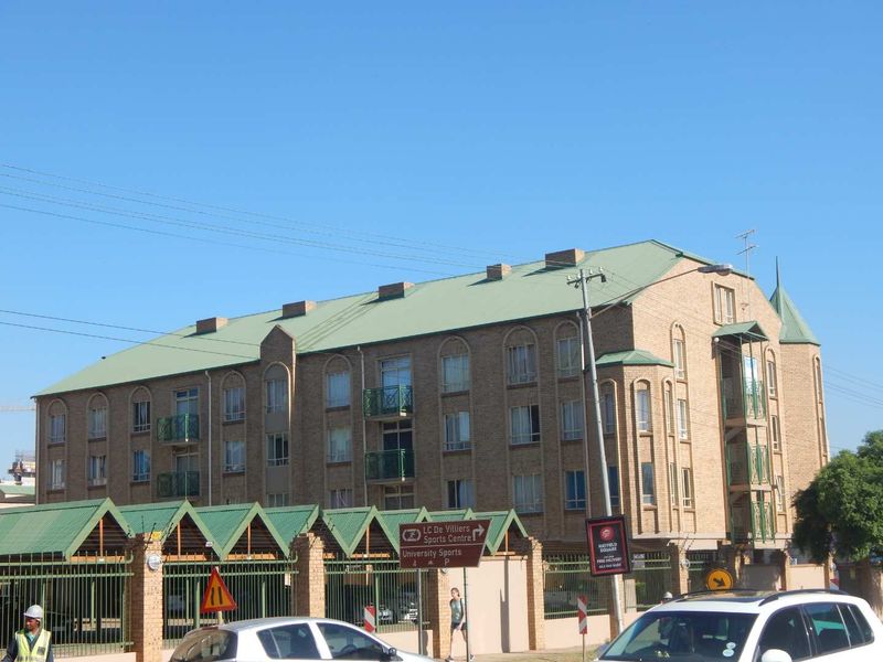 Exterior view of a multi-story brick apartment building featuring a pitched green metal roof and private balconies.