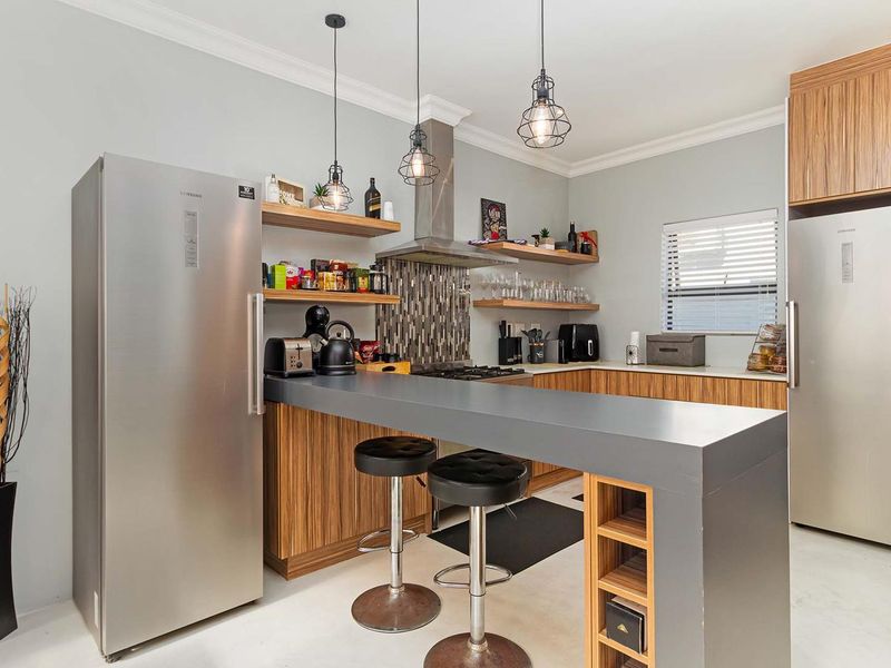 Modern kitchen featuring wood-grain cabinetry, stone countertops, a breakfast bar, gas hob with extractor fan, and stylish pendant lighting.