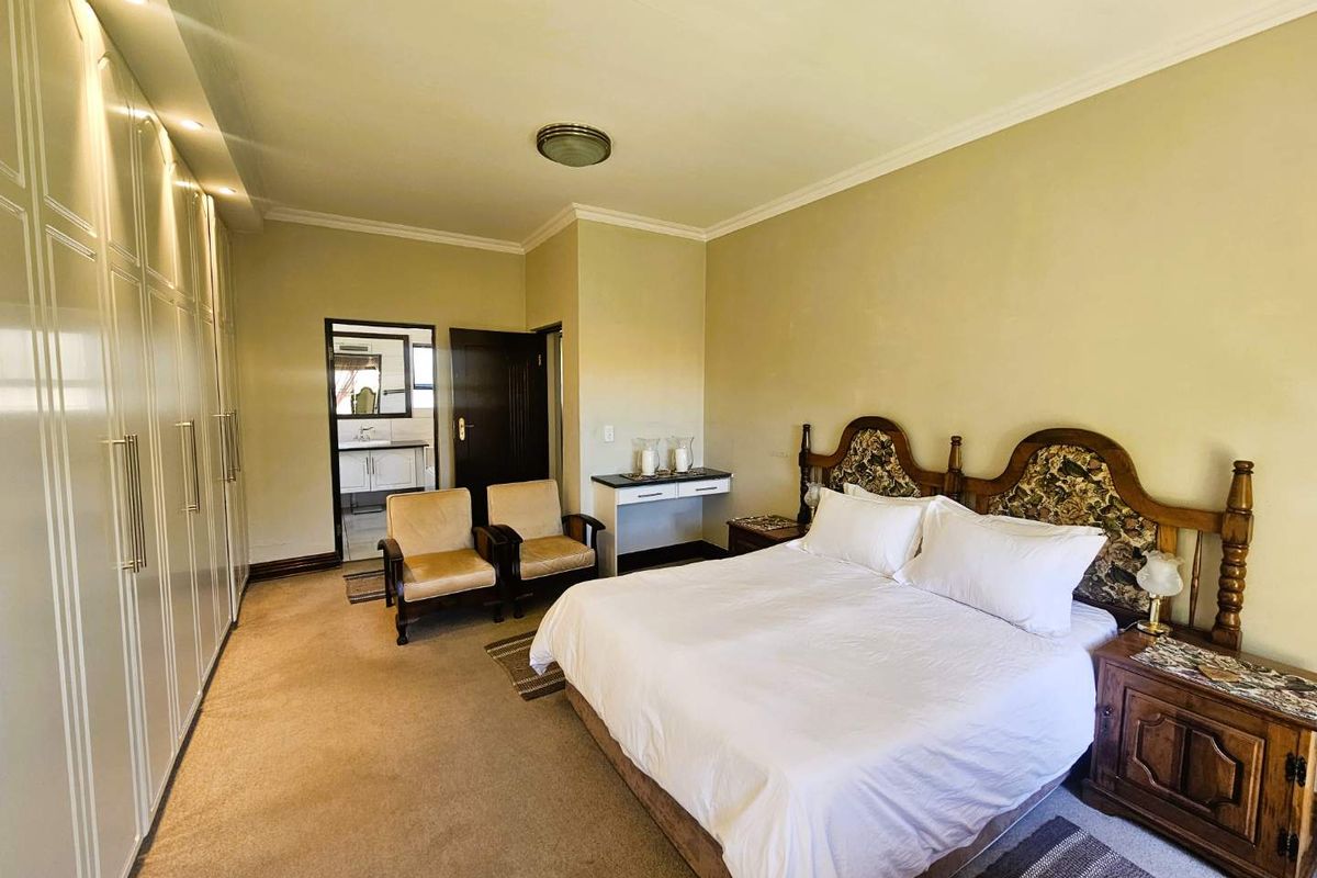 Spacious bedroom featuring extensive built-in cabinetry, neutral carpeting, and an adjoining en-suite bathroom.