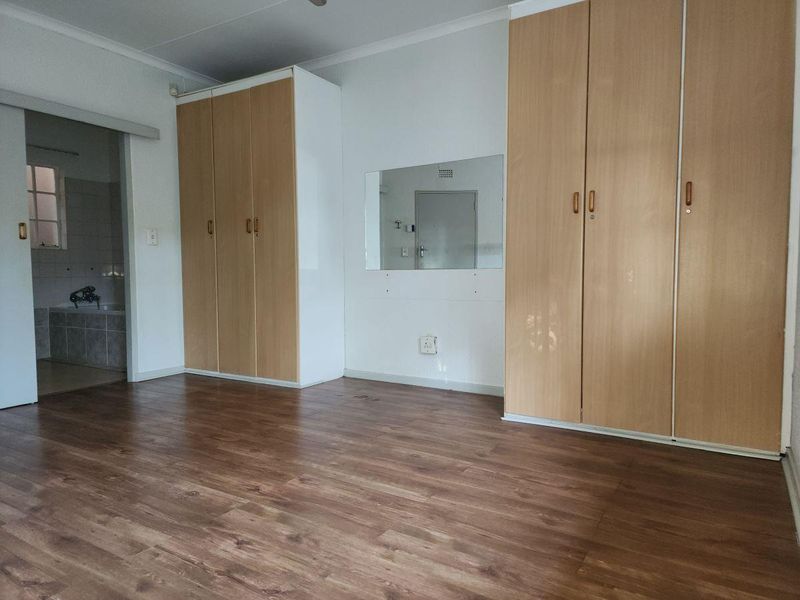 A spacious bedroom featuring laminate flooring, ample built-in cupboard storage, and direct access to an en-suite bathroom through a sliding door.