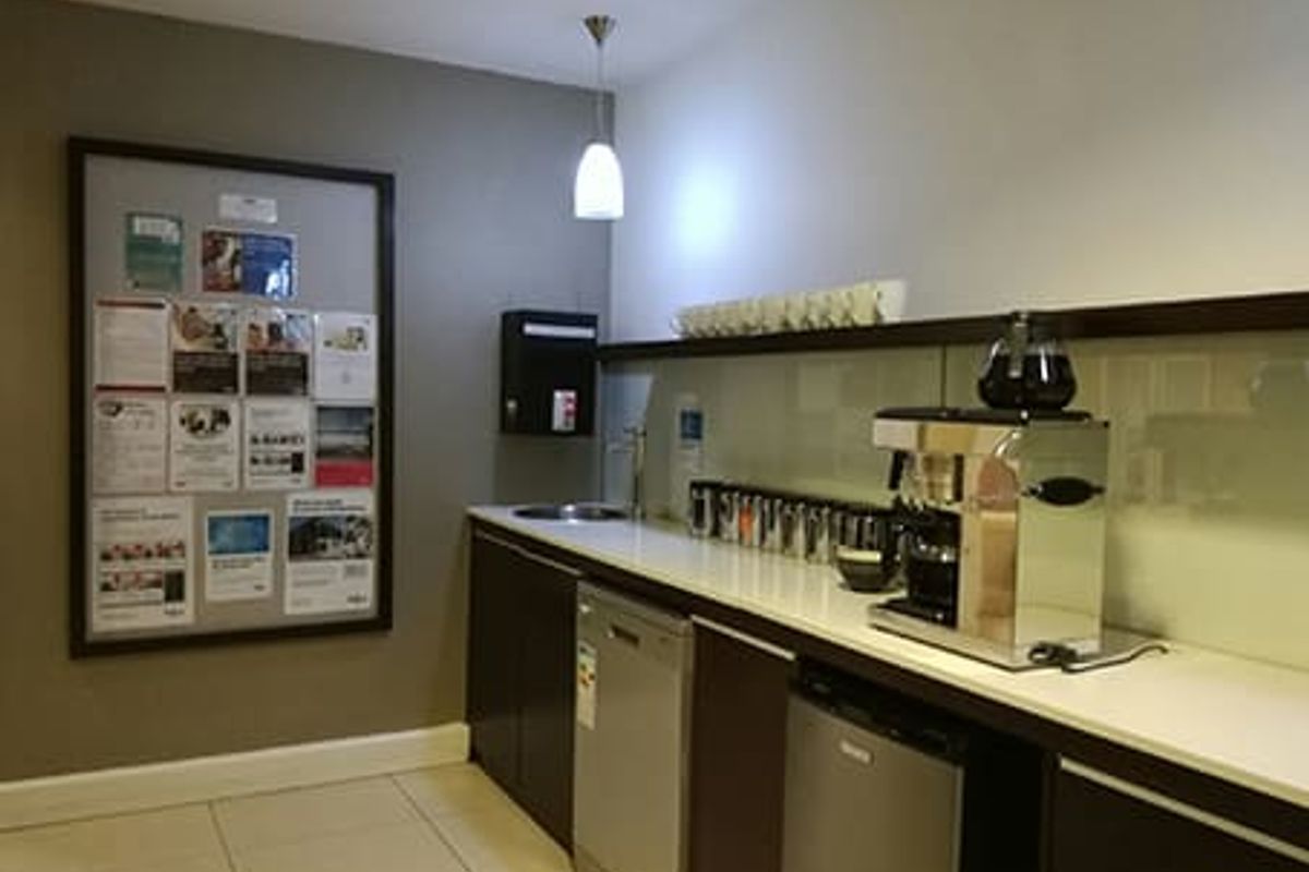 A functional office kitchenette featuring built-in cabinetry, a sink, integrated dishwasher, and a glass splashback.