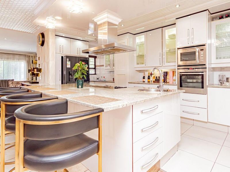 Spacious open-plan kitchen featuring granite countertops, integrated appliances, modern cabinetry, and a central island with breakfast bar seating, flowing into the living area.