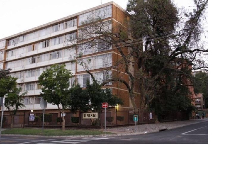 Street view of a multi-story brick apartment building with large windows and perimeter fencing.