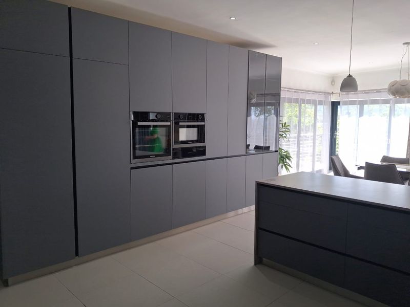 Modern kitchen featuring sleek handleless grey cabinetry, integrated appliances, a central island, and large sliding doors leading to an outdoor area.