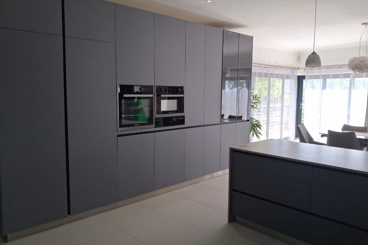 Modern kitchen featuring sleek handleless grey cabinetry, integrated appliances, a central island, and large sliding doors leading to an outdoor area.