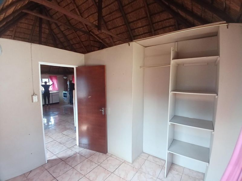 A bedroom featuring a traditional thatch roof, tiled flooring, and built-in storage shelving, with an open doorway leading to an adjacent living area.