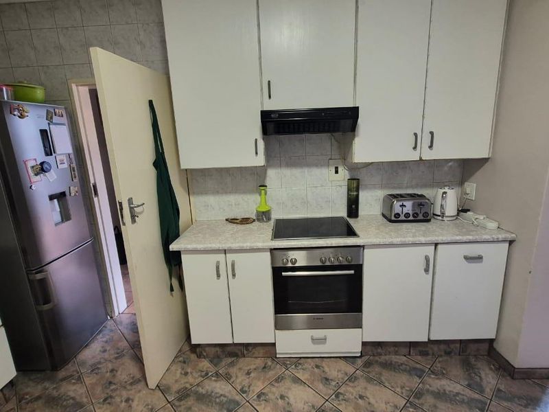 A functional kitchen featuring white built-in cabinetry, a tiled backsplash, and integrated electric cooking appliances with tiled flooring throughout.