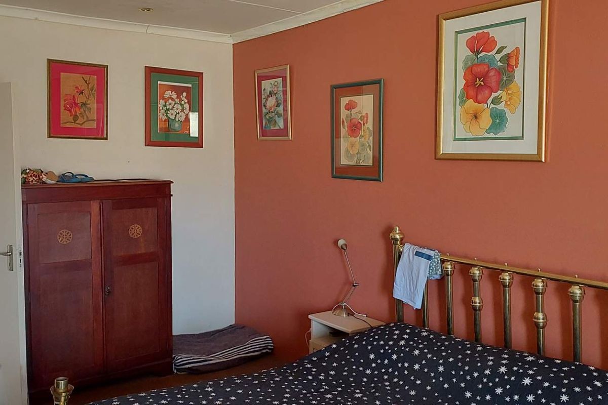 A bedroom featuring a terracotta-colored accent wall, neutral wall finishes, and a doorway leading to an adjacent room.