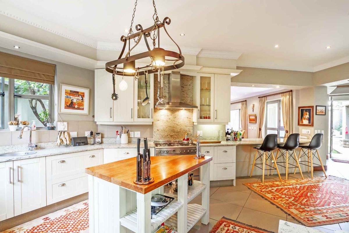 A well-appointed kitchen featuring shaker-style cabinetry, stone countertops, a central island with a wooden top, and a stainless steel gas range with extractor fan.