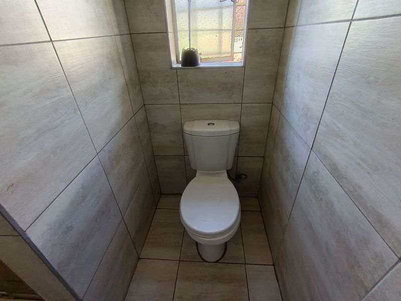 A compact, fully tiled bathroom featuring a modern toilet and a small window for natural light.