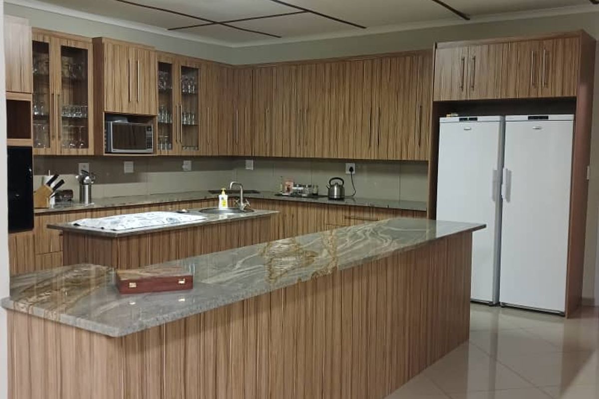Spacious kitchen featuring wood-grain cabinetry, granite countertops, a central island with breakfast bar, and tiled flooring.