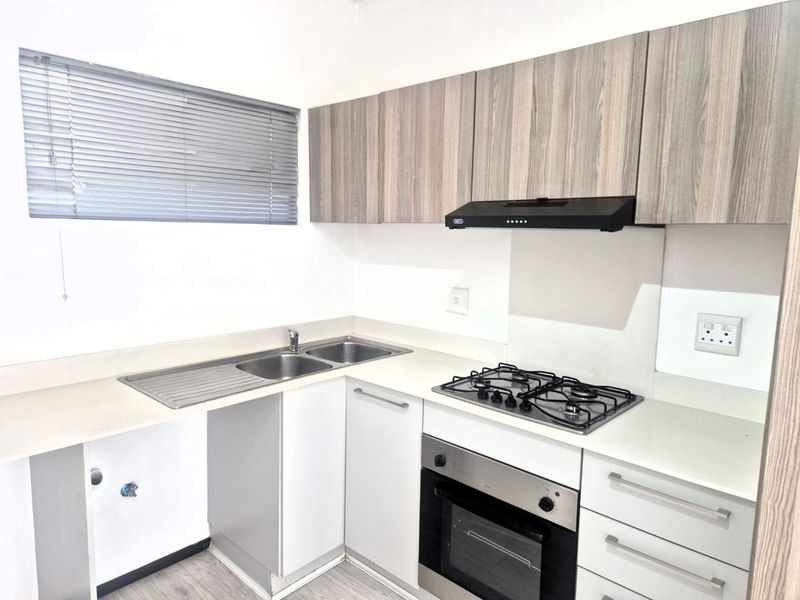A modern, clean kitchen featuring light wood-tone cabinetry, a gas hob, built-in oven, extractor fan, and a stainless steel double sink.
