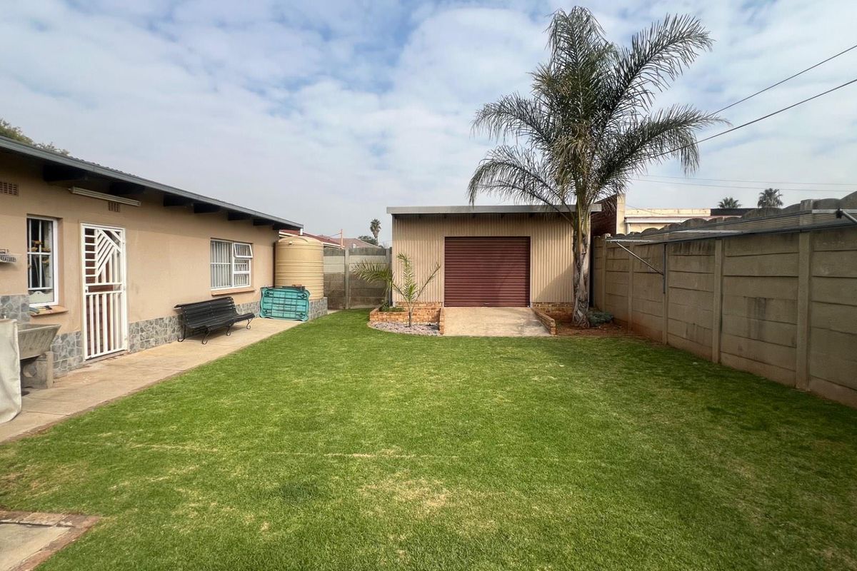 A spacious rear garden featuring a well-maintained lawn, a detached garage, and a water storage tank, enclosed by secure boundary walls.