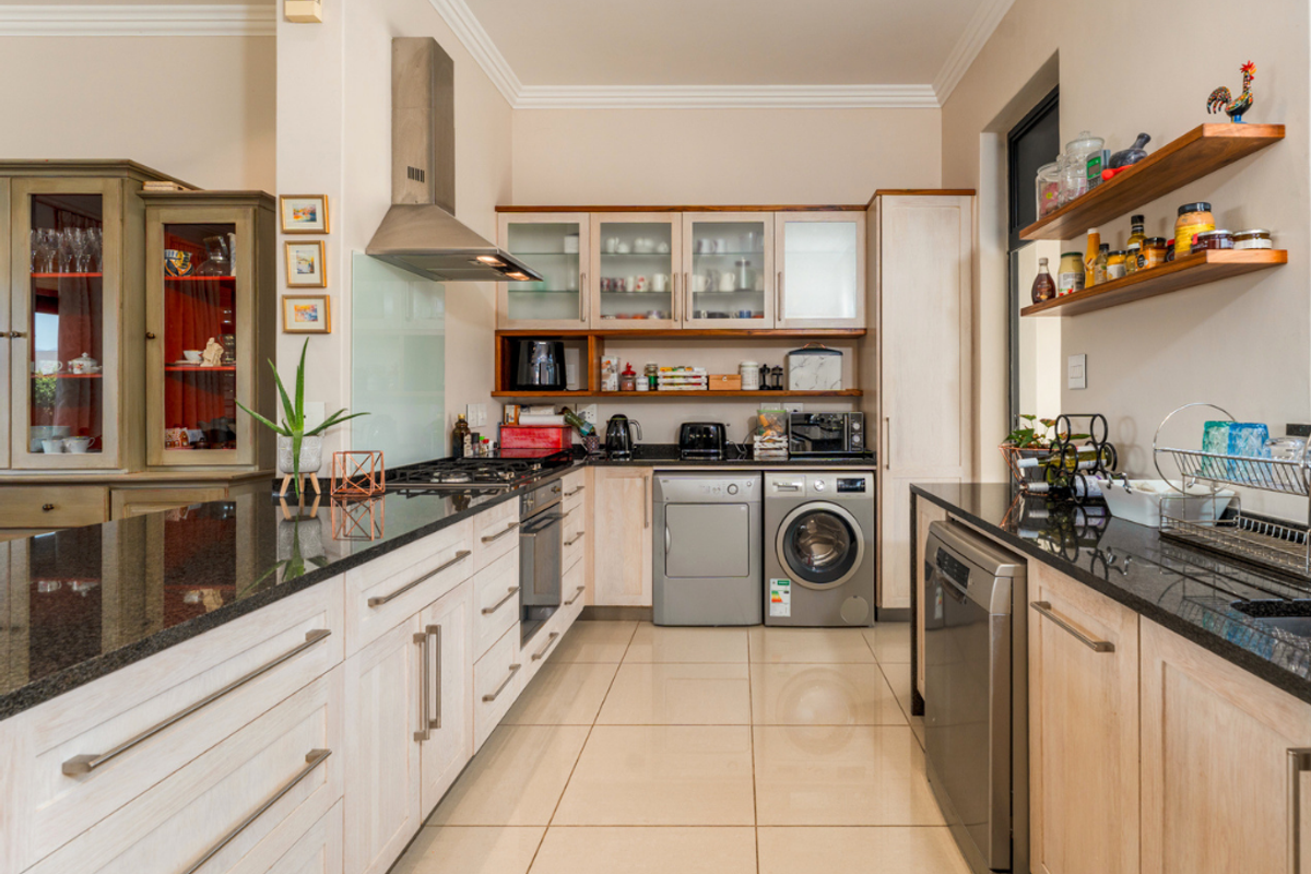 A well-appointed kitchen featuring light wood cabinetry, dark granite countertops, stainless steel appliances, and tiled flooring with recessed ceiling lighting.