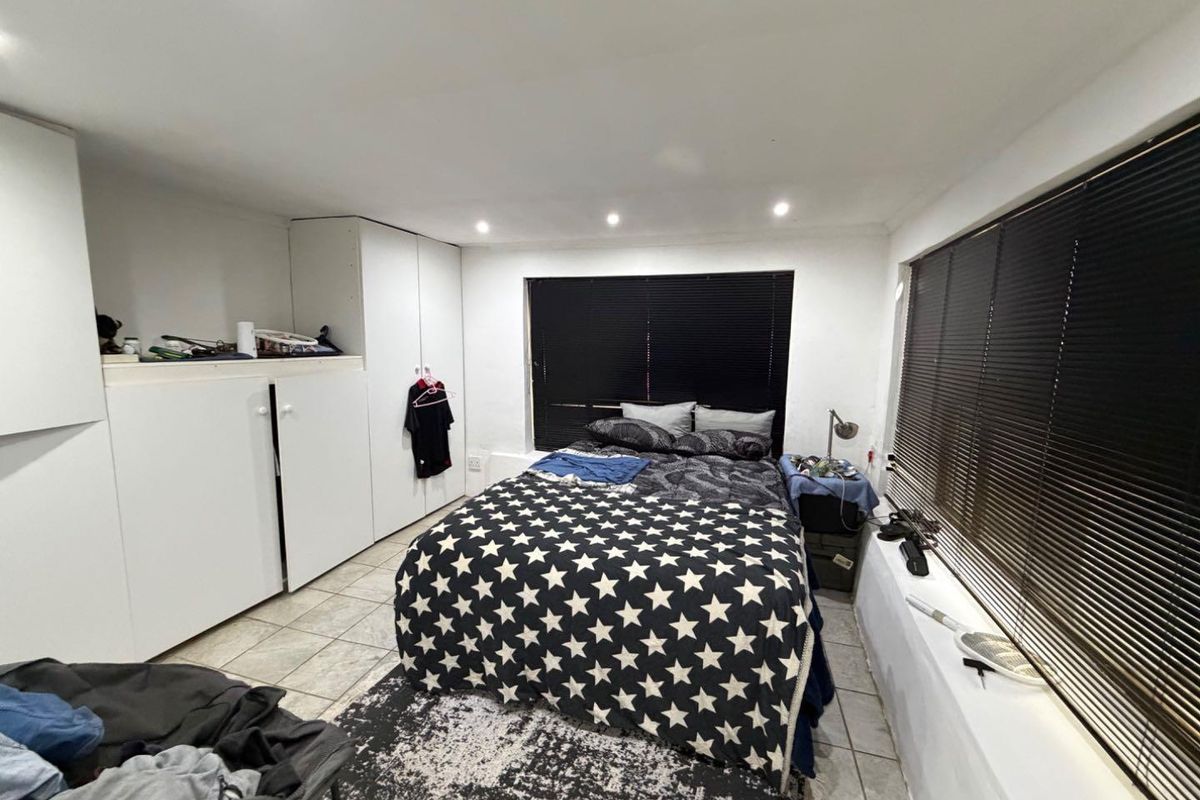 A bedroom featuring tiled flooring, built-in cupboards, and recessed downlights, with large windows fitted with venetian blinds.