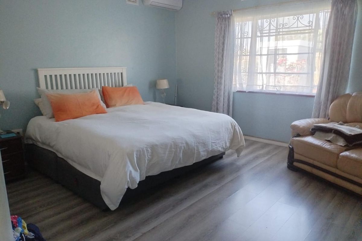 A bedroom featuring light blue walls, laminate flooring, and a wall-mounted split-system air conditioner.