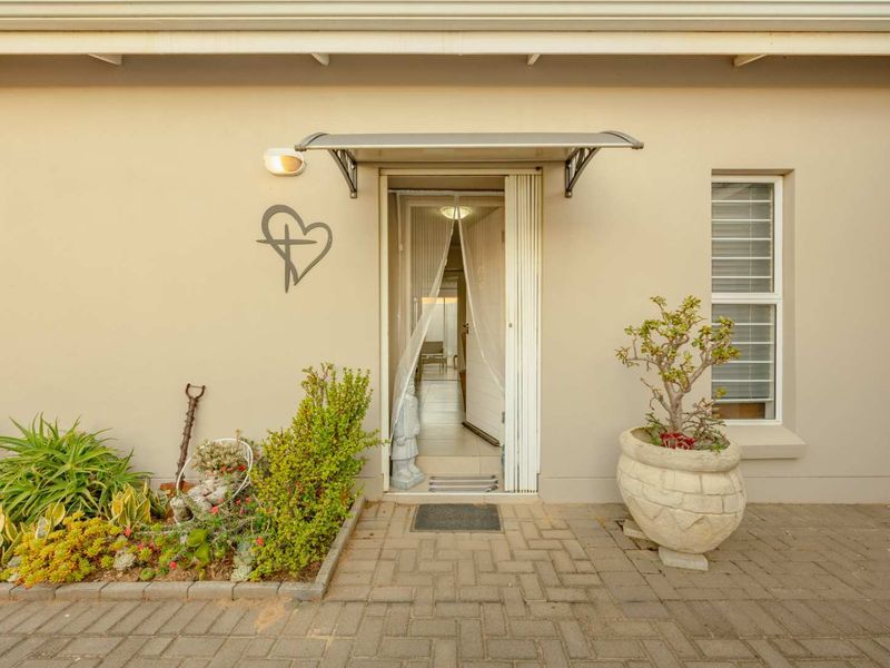 A well-maintained rear exterior view featuring a paved patio area, a protective awning over the entrance, and a secure louvre window.