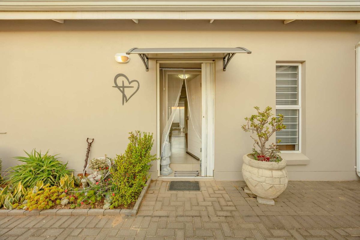 A well-maintained rear exterior view featuring a paved patio area, a protective awning over the entrance, and a secure louvre window.