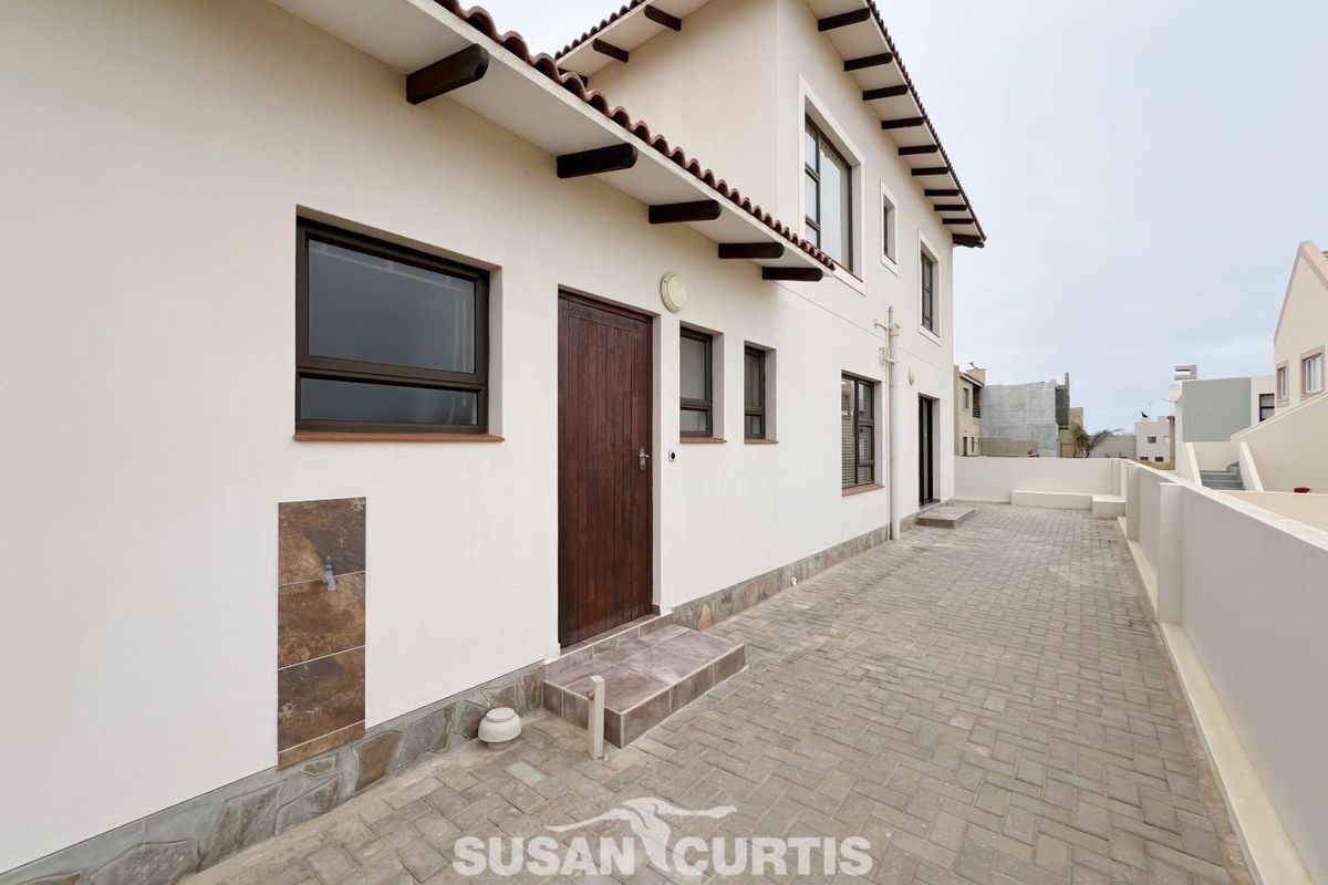 A view of the rear exterior of the house, featuring paved patio area, tiled roof eaves, and external wall-mounted water tap.