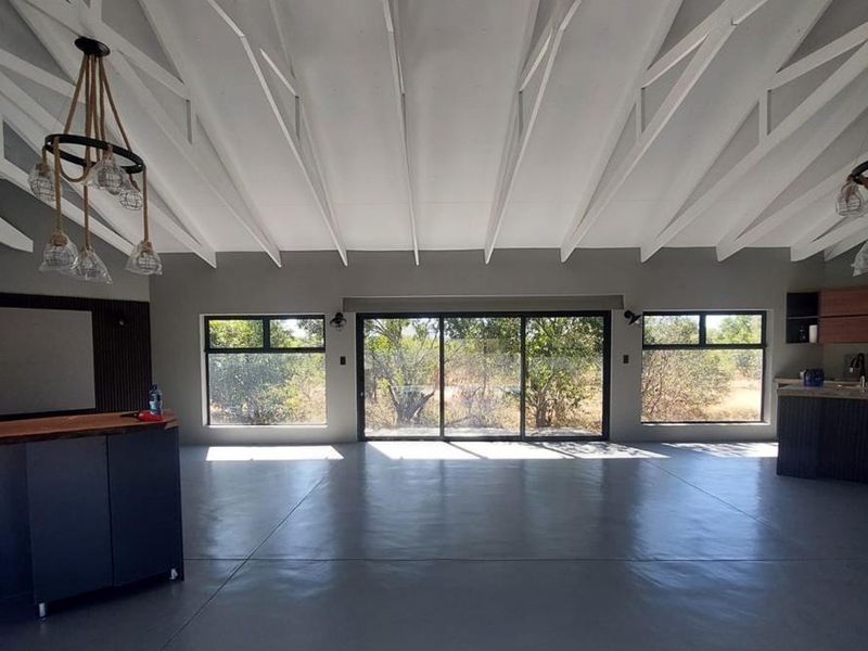 Spacious open-plan living area featuring high vaulted ceilings with exposed trusses, polished concrete floors, and large sliding doors opening to the exterior.
