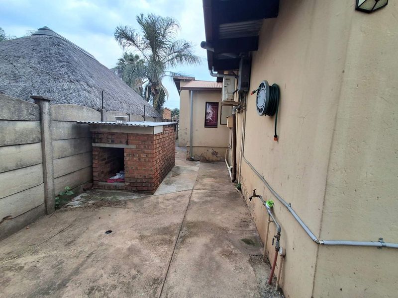 Rear exterior area featuring a brick built-in braai, concrete paving, and external utility fixtures along the side of the house.