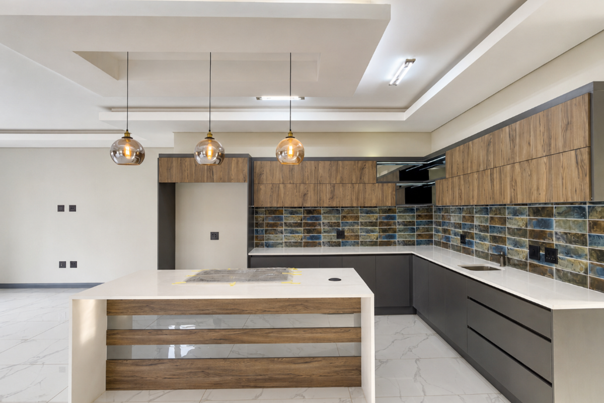 Modern, spacious kitchen featuring a large island, sleek wood-grain and charcoal cabinetry, stone countertops, and a decorative tiled backsplash.