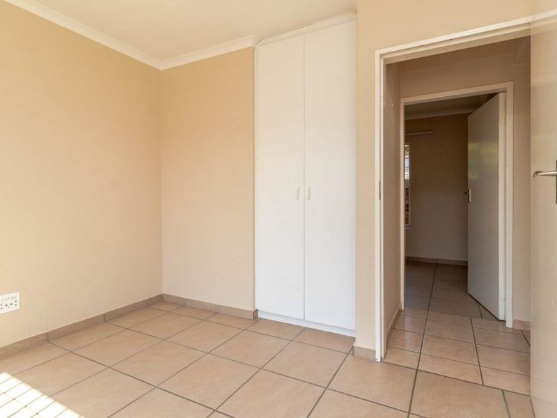 An empty bedroom featuring neutral wall paint, tiled flooring, and a built-in wardrobe, with an open doorway leading to an adjacent space.