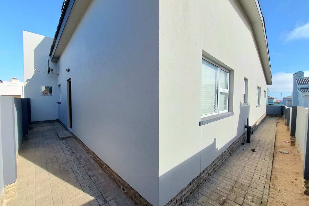 Side exterior view of the house featuring paved walkways, smooth rendered walls, and white-framed windows.