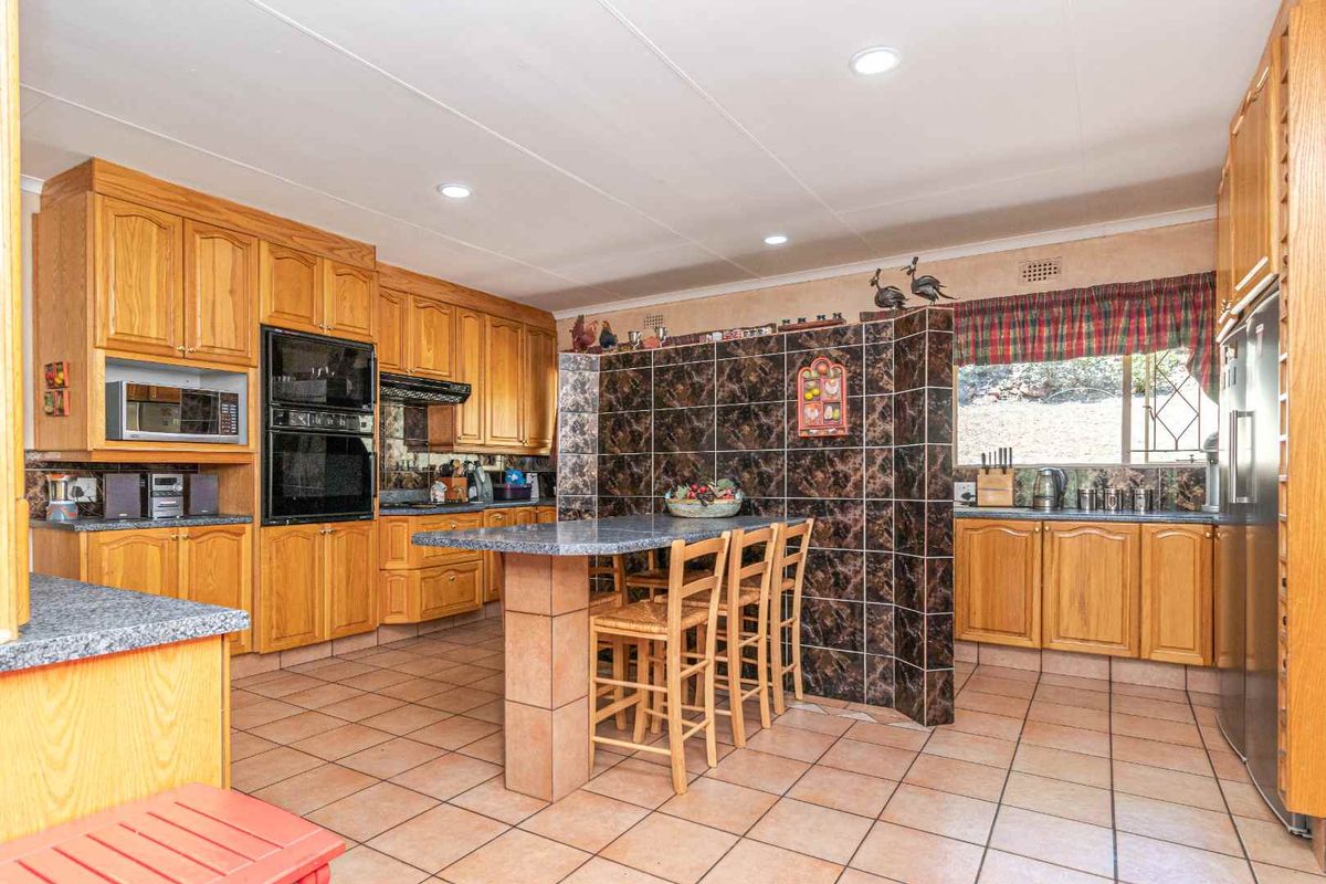 Spacious kitchen featuring traditional timber cabinetry, granite-look countertops, a central breakfast island, and integrated wall-mounted oven and microwave.