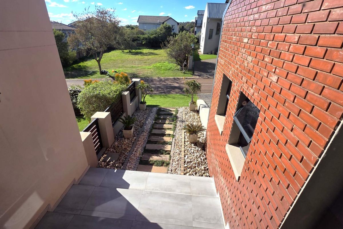 An elevated view looking down from a tiled landing towards a landscaped garden path with stone features and brick walling.
