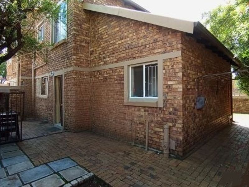 Rear exterior view of the townhouse featuring a face brick facade, paved patio area, and secure window installations.