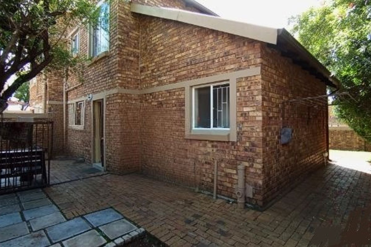 Rear exterior view of the townhouse featuring a face brick facade, paved patio area, and secure window installations.
