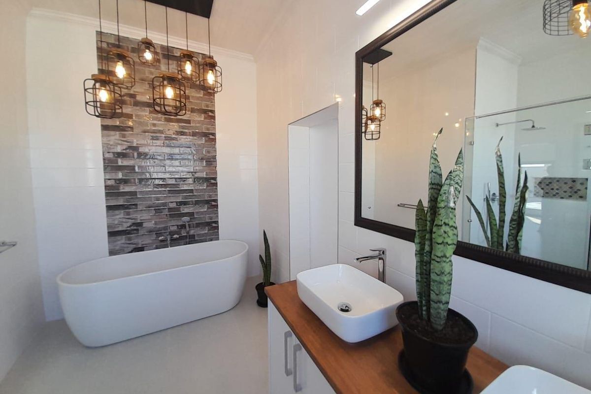 Modern bathroom featuring a freestanding bathtub, dual vessel sinks on a wooden vanity, and a decorative tiled feature wall with industrial-style pendant lighting.