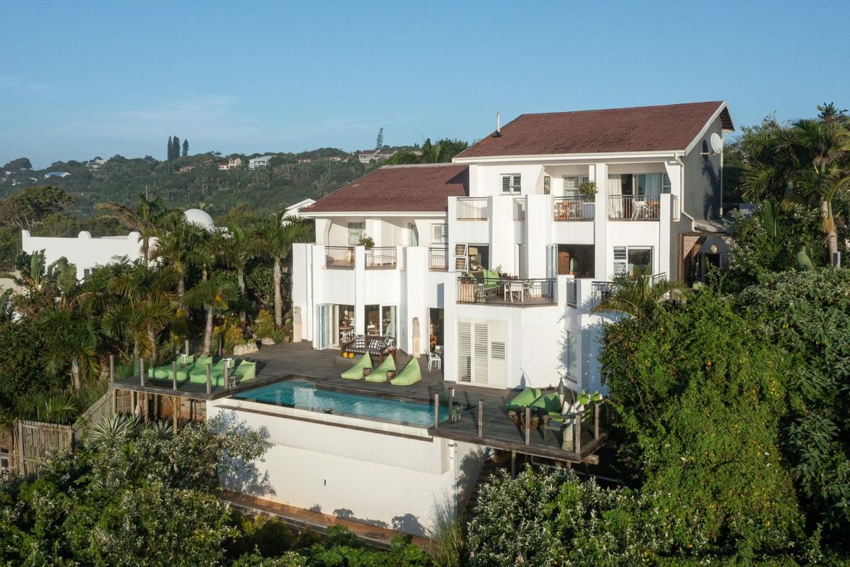 Aerial view of a multi-level residential property featuring a swimming pool, expansive timber decking, and multiple balconies set within a lush landscaped environment.