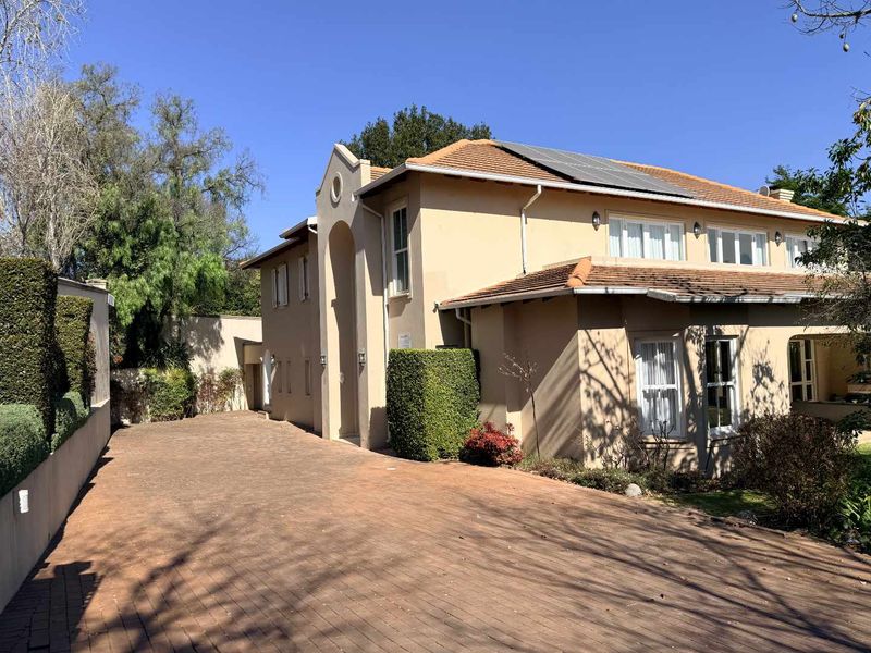 A well-maintained double-story residential property featuring a paved driveway, tiled roof with solar panels, and established garden landscaping.