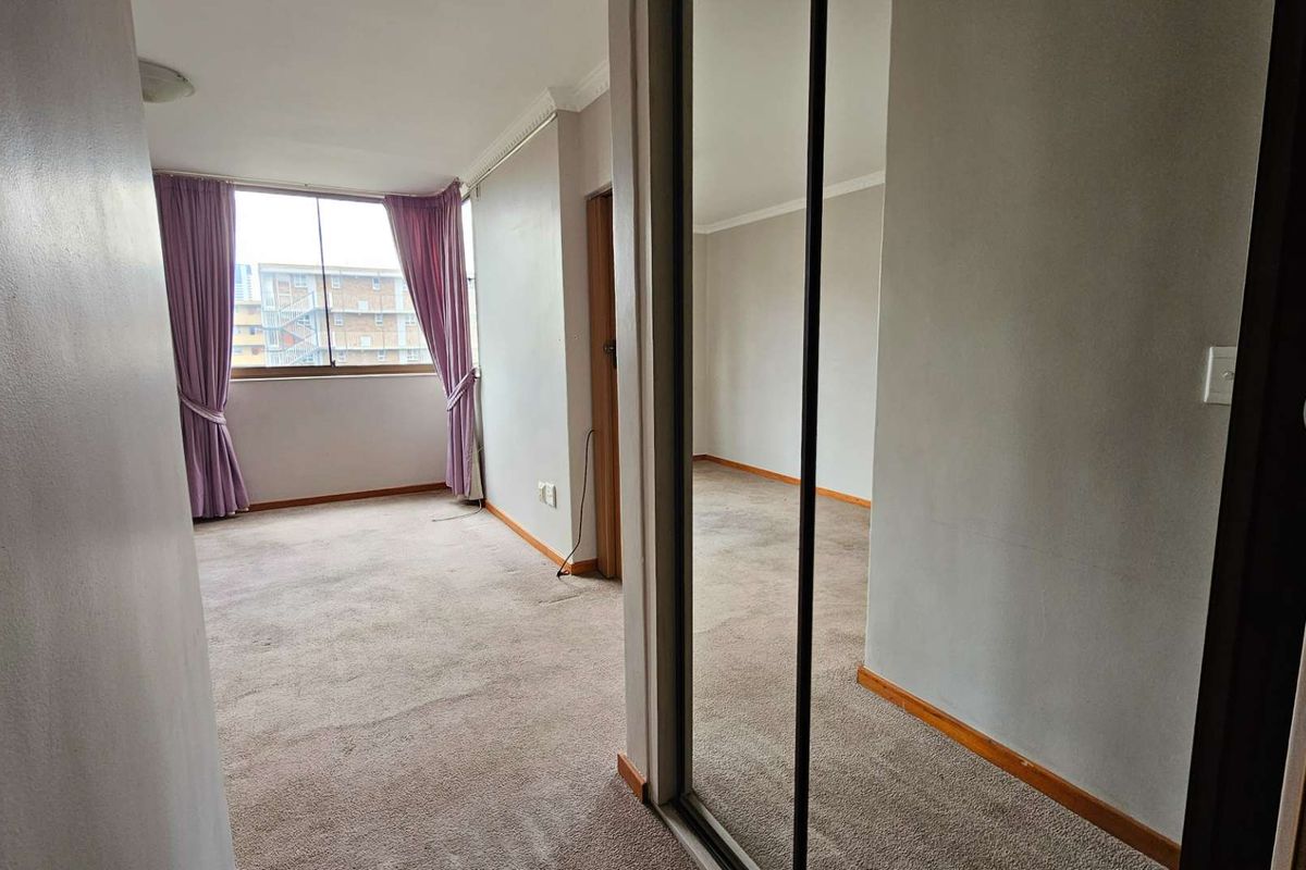 A bedroom featuring built-in mirrored wardrobes, neutral wall finishes, and large windows allowing for natural light.