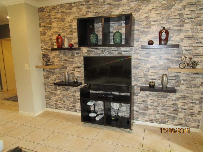 Living room featuring a stone veneer accent wall with integrated shelving units and neutral tiled flooring.