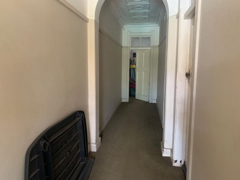 A long hallway featuring a classic archway, decorative pressed metal ceiling, and original architectural details, currently presenting in need of cosmetic refurbishment.