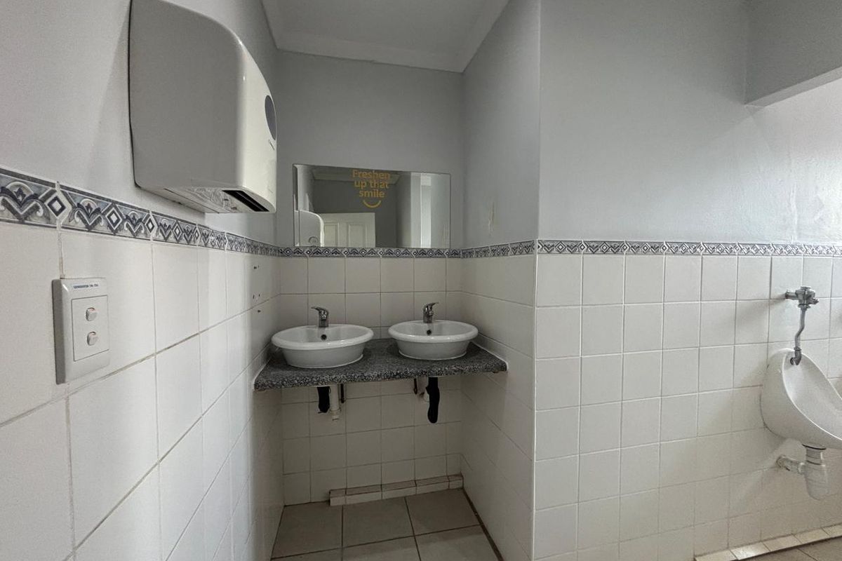 A functional office restroom featuring dual vanity basins, a wall-mounted urinal, and tiled wall finishes with a decorative border.