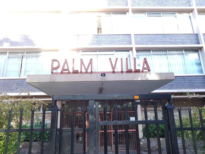 Front entrance view of Palm Villa apartment building featuring a metal security gate and concrete canopy.
