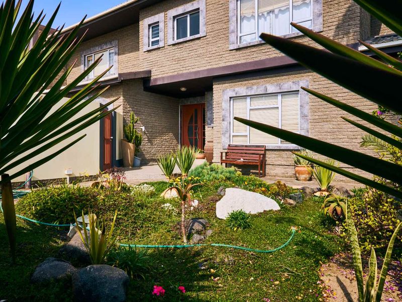 Front elevation of a two-story brick house featuring a landscaped garden, paved entrance path, and traditional window detailing.